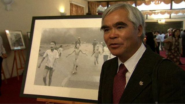 Nick Út đứng cạnh bức ảnh Em bé Napalm tại triển lãm ảnh AP ở Hà Nội