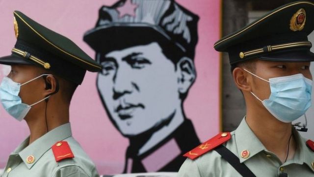 Chinese police officers wearing face masks in front of an image of a man wearing a cap with a red star