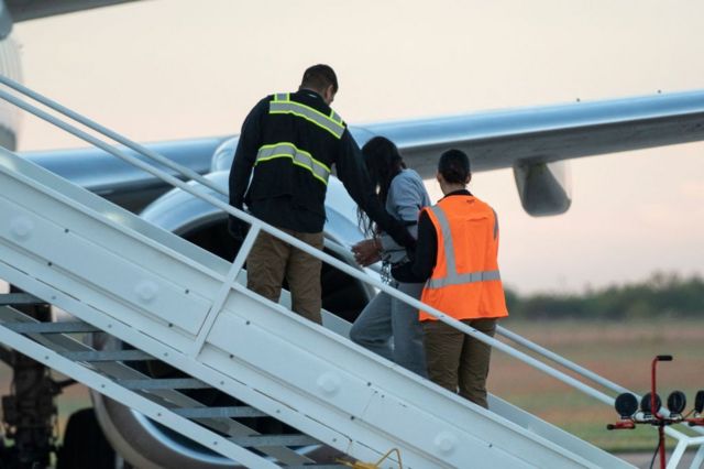 Una mujer sube custodiada a un avión de deportados venezolanos. 