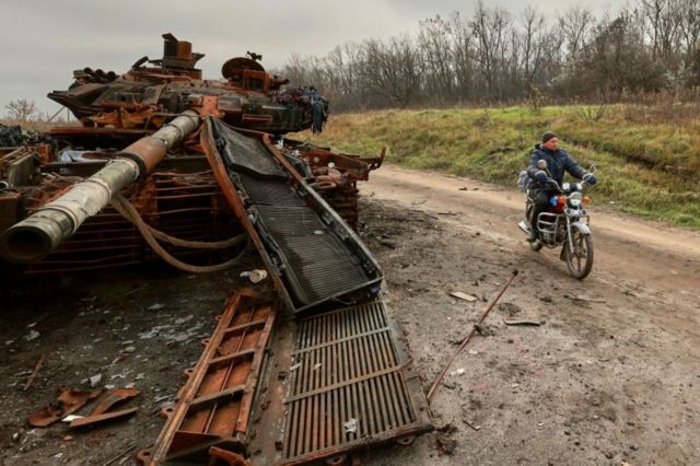 Một người đàn ông địa phương đi xe máy ngang qua một chiếc xe tăng bị phá hủy ở vùng Kharkiv, Ukraine, ngày 09 tháng 11 năm 2022