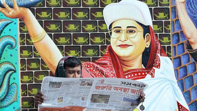 বাংলাদেশী পাঠক তৎকালীন বিরোধী নেতা শেখ হাসিনার পোস্টারের সামনে জরুরী অবস্থার খবর জানছেন, ১২-০১-২০০৭।