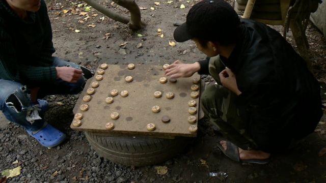 Two men play a game as they wait at the camp