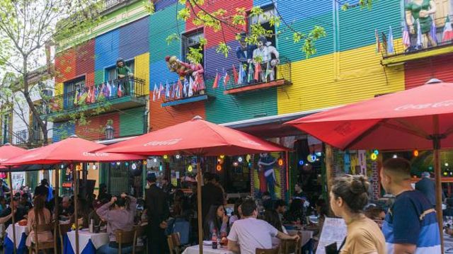 Pessoas em restaurante com área externa, com paredes coloridas típicas do Caminito