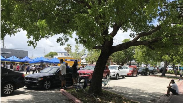 Autos en fila esperan que empiece la distribución gratuita de alimentos