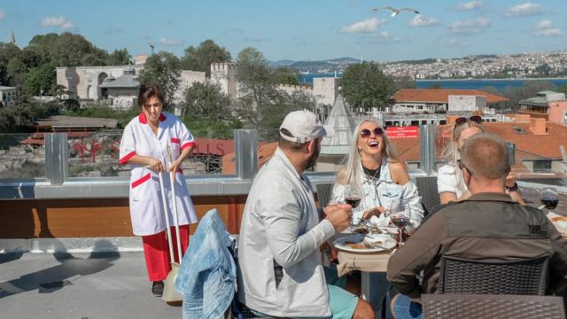 مجموعة من السياح يتناولون وجبة في اسطنبول بينما تقف عاملة نظافة على مقربة منهم