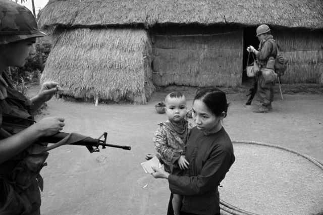 A soldier pointing a gun at a mother and child