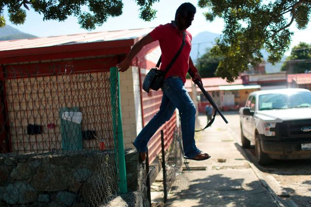 Un civil armado en México saltando una reja.