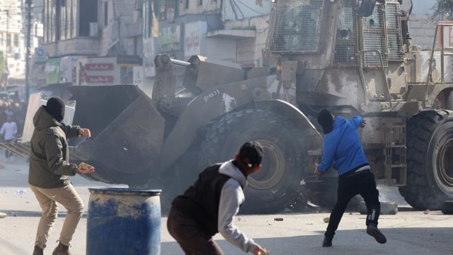 Palestinos jogam pedras em meio a confrontos com tropas israelenses durante um ataque em Jenin