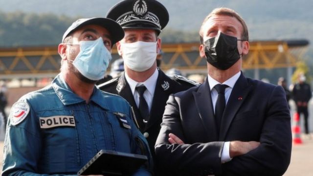 الرئيس الفرنسي إيمانويل ماكرون وفردان من الشرطة الفرنسية يلبسون أقنعة واقية