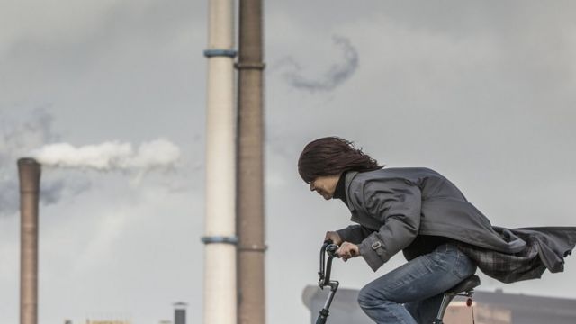 Una persona en bicicleta con fábricas detrás.