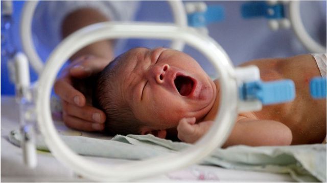 A baby yawns or cries in an incubator