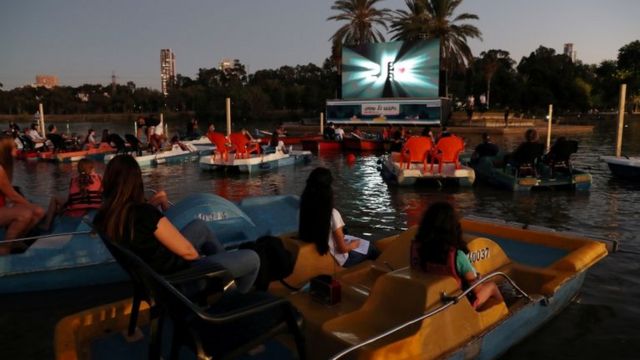 Groups in boats on the lake in the afternoon, with a movie screen in the background