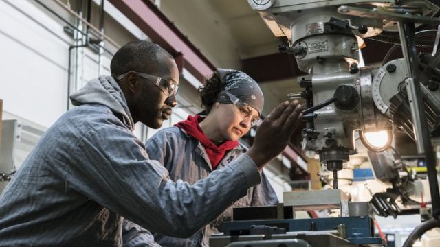 Dos trabajadores usan un taladro en una fábrica