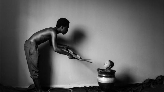 صورة من سلسلة تحمل اسم لجوء للمصور إيريك غيامفي من غانا تظهر رجلا يحمل مقص الزرع ويقترب من طفل في وعاء