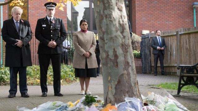 Boris Johnson (L) stands with with Chief Constable of Essex Police, Ben-Julian Harrington (2L), and Britain's Home Secretary Priti Patel (C) after they laid flowers