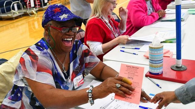 An election worker hands over a voting receipt wearing a stars and stripes outfit
