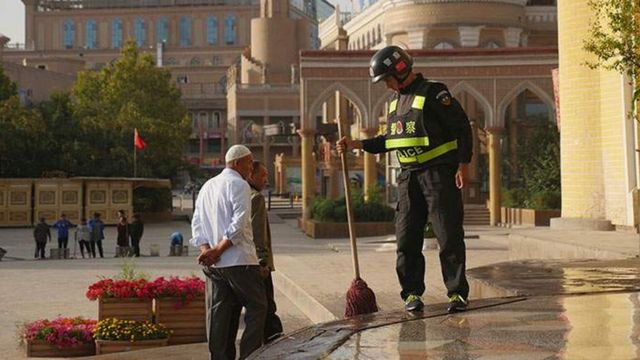 Policial chinês limpando escadas de mesquita na cidade de Kashgar