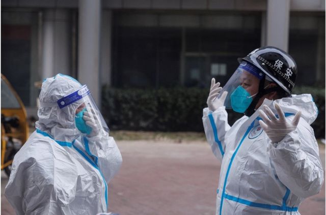 Anti-epidemic workers in protective suits prepare to enter a cordoned-off apartment building.
