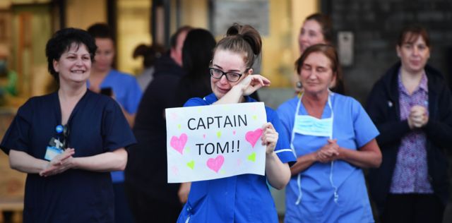 NHS staff in Liverpool clapping for key workers, with one holding a sign in support of Captain Tom Moore