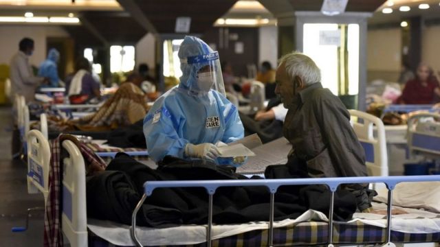 Profissional de saúde paramentado atende idoso em hospital de Nova Déli