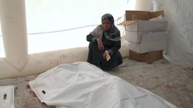 A woman sits next to the bodies of some of her relatives killed in an Israeli bombardment