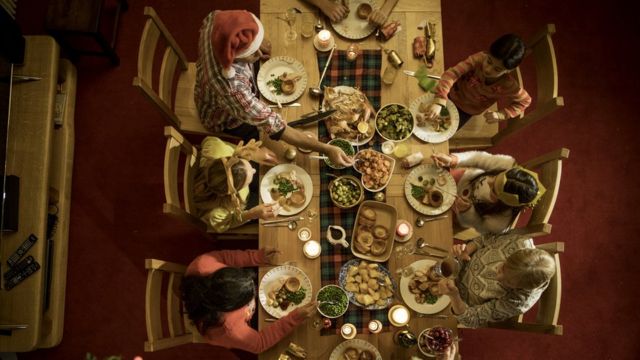 Mesa com ceia de natal e família sentada ao redor vista do alto