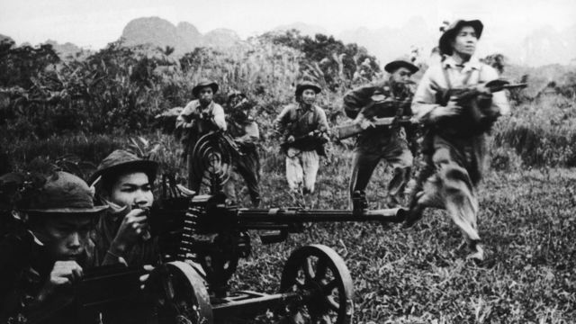 Viet Cong soldiers moving forward under covering fire from a heavy machine gun during the Vietnam War, circa 1968