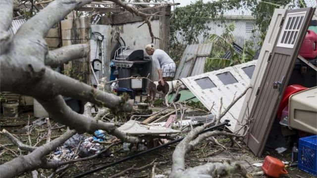 Una mujer con su perro recorre lo que quedó de su casa en Puerto Rico.
