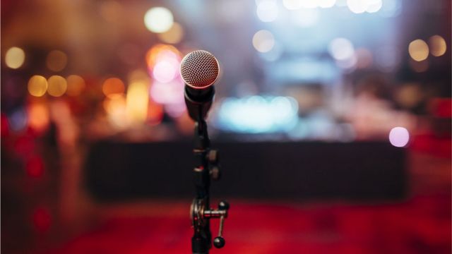 A microphone on a stage waiting for a speaker, with audience in blurred background