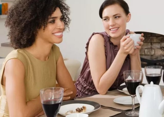 Deux femmes en sourire avec des verres de vin sur la table.
