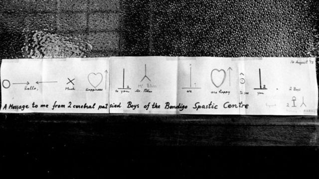 Mensagem em símbolos de Bliss entregue ao seu criador em 1974, assinada por dois meninos com paralisia cerebral do Centro Espástico Bendigo, na Austrália: “olá, muita felicidade para você, sr. Bliss, estamos felizes por vê-lo”