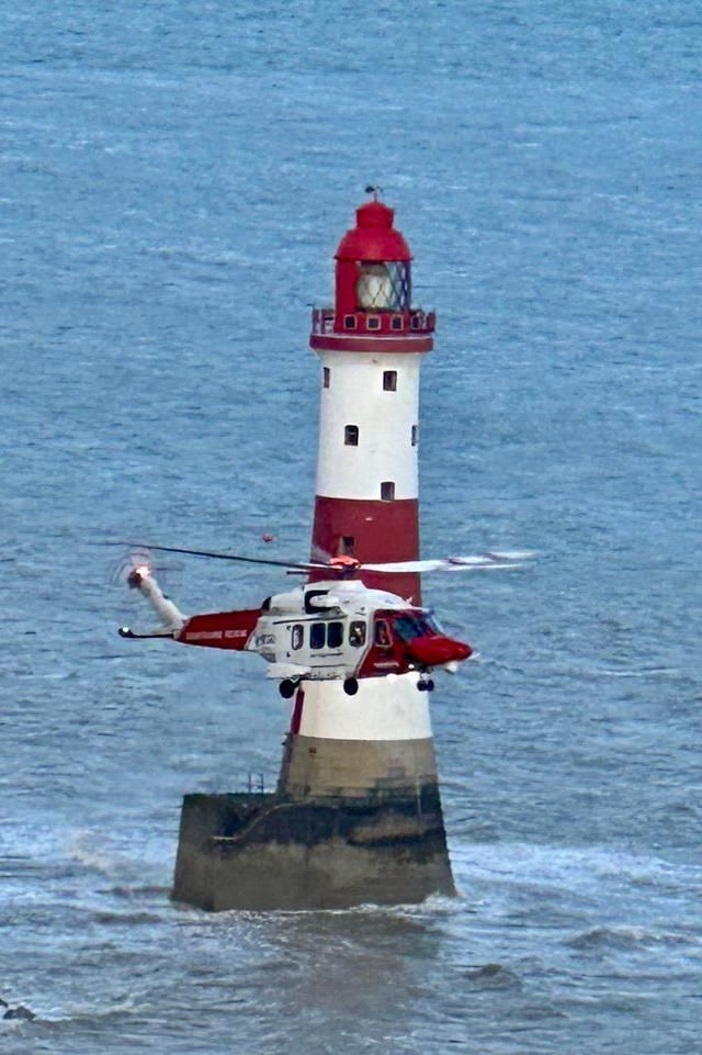 A helicopter flying in front of a lighthouse 