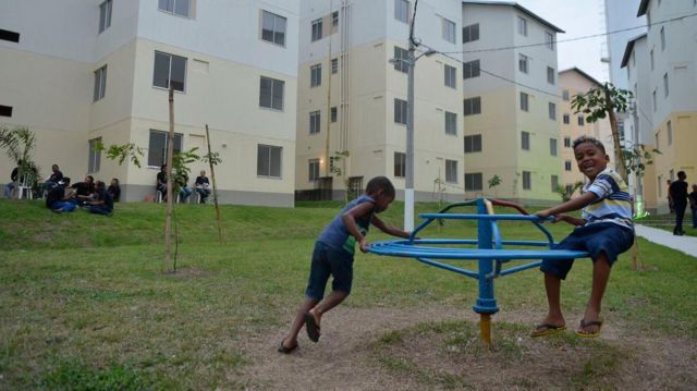 Meninos brincando em gira-gira próximos a edifícios de conjunto habitacional popular