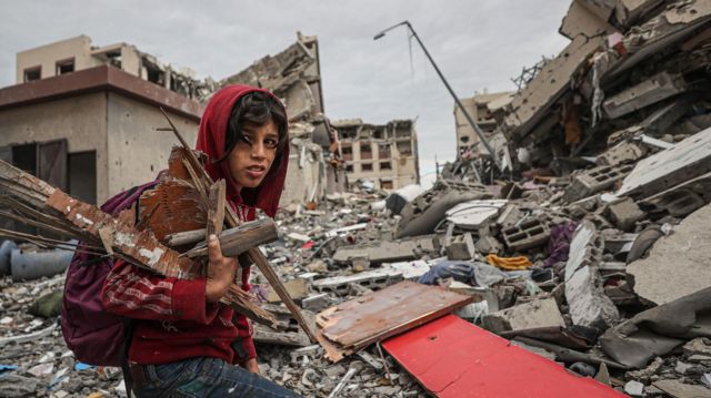 Un niño recoge leña entre edificios destruidos en Gaza