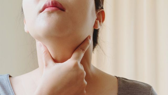 Uma mulher usa os dedos para sentir parte do pescoço