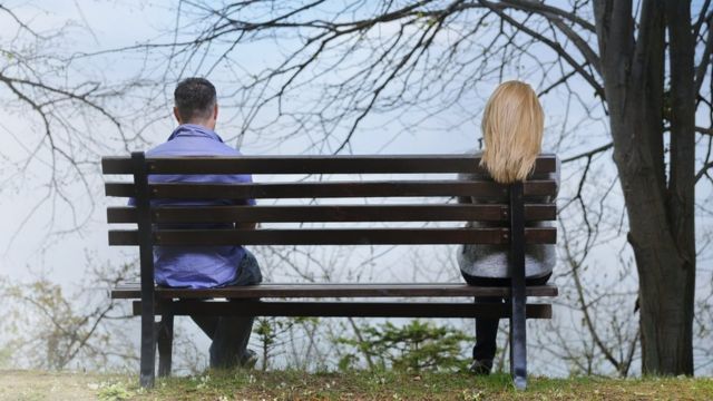 Casal sentado separadamente em um banco