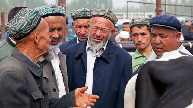Uyghur farmers wearing doppas, trading cows at the cattle market in Kashgar