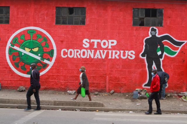 Pessoas no Quênia passam diante de um grafite em um muro retratando o coronavírus