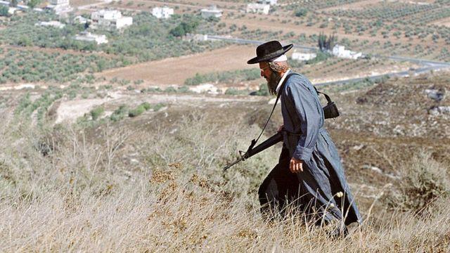 مستوطن يهودي مسلح يسير في حقل بالضفة الغربية المحتلة