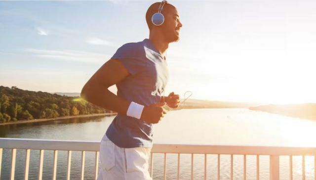 Homem correndo usando fones de ouvido com rio ao fundo