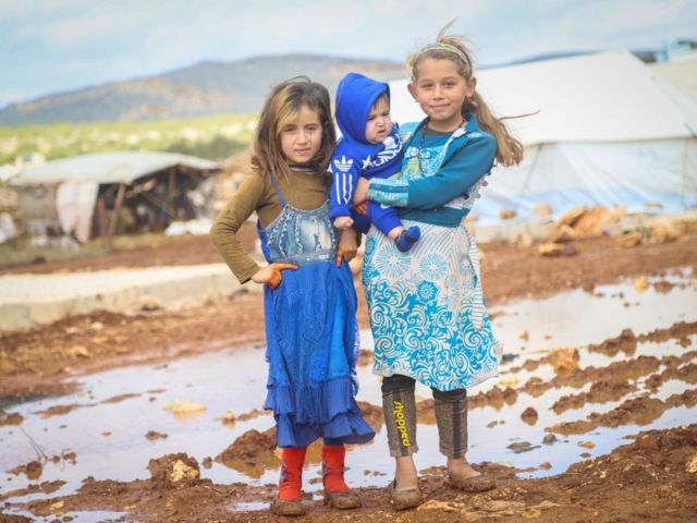 أطفال سوريون يقفون لالتقاط صورة في الوحل بعد أن تسببت الأمطار الغزيرة في إلحاق أضرار بمخيمهم في إدلب ، سوريا في 15 يناير / كانون الثاني 2021.