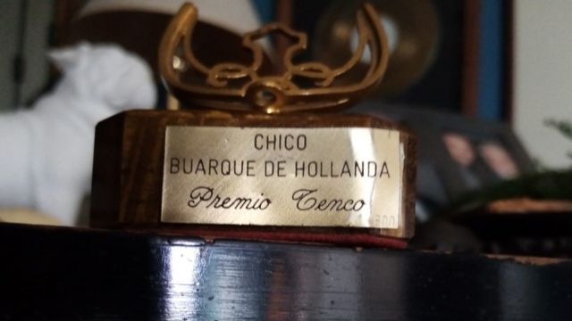 Trofeú em cima da mesa diz: Chico Buarque de Hollanda, troféu Tenco