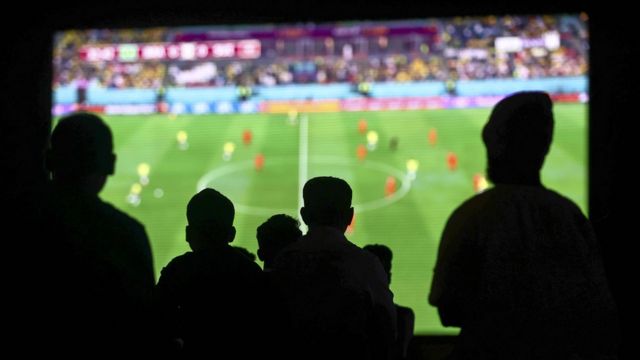 Migrant workers follow the FIFA World Cup 2022 matches at a giant screen set up at a cricket stadium in Doha