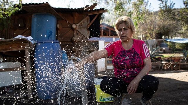 Luz Valdebenito com torneira aberta em seu quintal abre uma torneira depois que um caminhão-tanque lhe entregou água em Til Til, Chile.