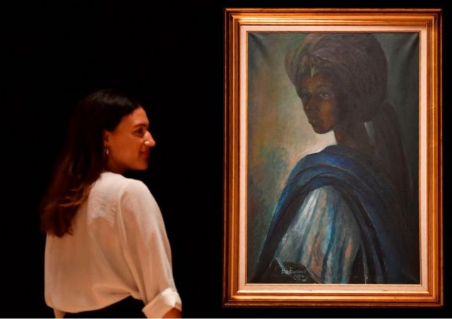 An employee poses with a work of art by Nigerian painter and sculptor Ben Enwonwu entitled 'Tutu' expected to realise 200,000-300,000 GBP (278000-417,000 USD) at auction in Bonhams auction house London on February 7, 2018. Tutu, a recently rediscovered portrait of the Ife royal princess Adetutu Ademiluyi painted in 1974 by the Nigerian artist Ben Enwonwu, leads Bonhams Africa Now sale in London on February 28. The painting, one of a series of three versions, once thought lost came to light after having gone unseen for decades in a north London flat. The whereabouts of the other two versions remains a mystery.