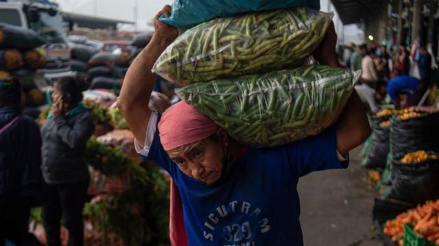 Un hombre carga sacos con verduras en un mercado peruano