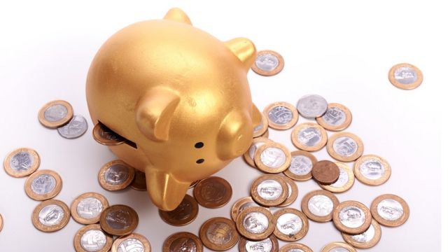 Cofrinho com moedas de real espalhadas