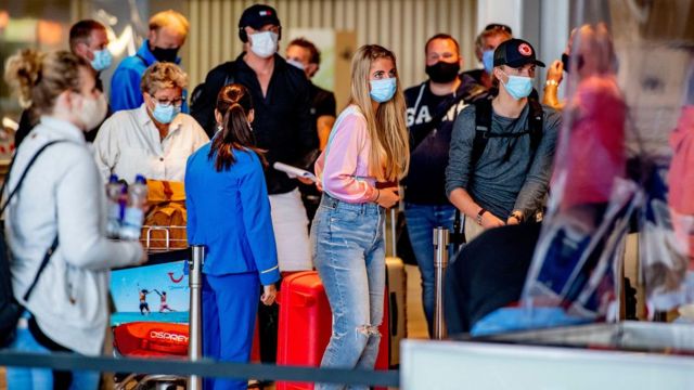 Pessoas de máscara em fila de aeroporto