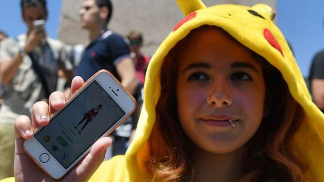 Una joven con un traje de Pikachu y su teléfono, en el que juega Pokémon Go