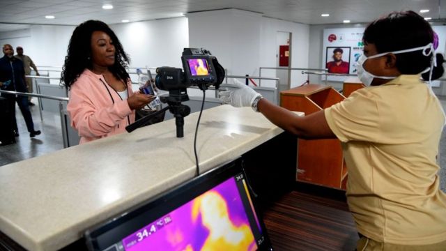A Port Health Service staff member stands next to a thermal scanner as passengers arrive at the Murtala Mohammed International Airport in Lagos,